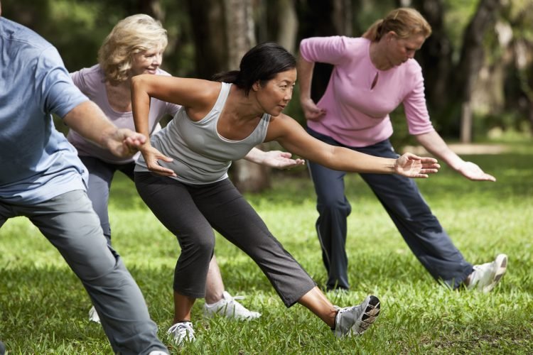 Multi-ethnic group of adults practicing tai chi in park.  Main focus on Asian woman.